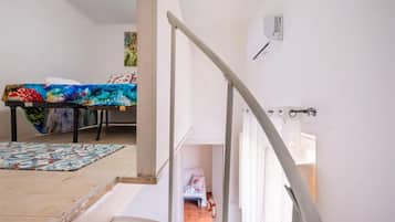 Eine Treppe führt zu einem Zimmer mit einem Bett, einem Tisch mit einer bunten Tischdecke und einem Gemälde an der Wand.