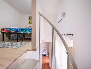 A staircase leading to a room with a bed, a table with a colorful tablecloth, and a painting on the wall. - Vista Sul Blu Private Residence 3 (Porto Cesareo)