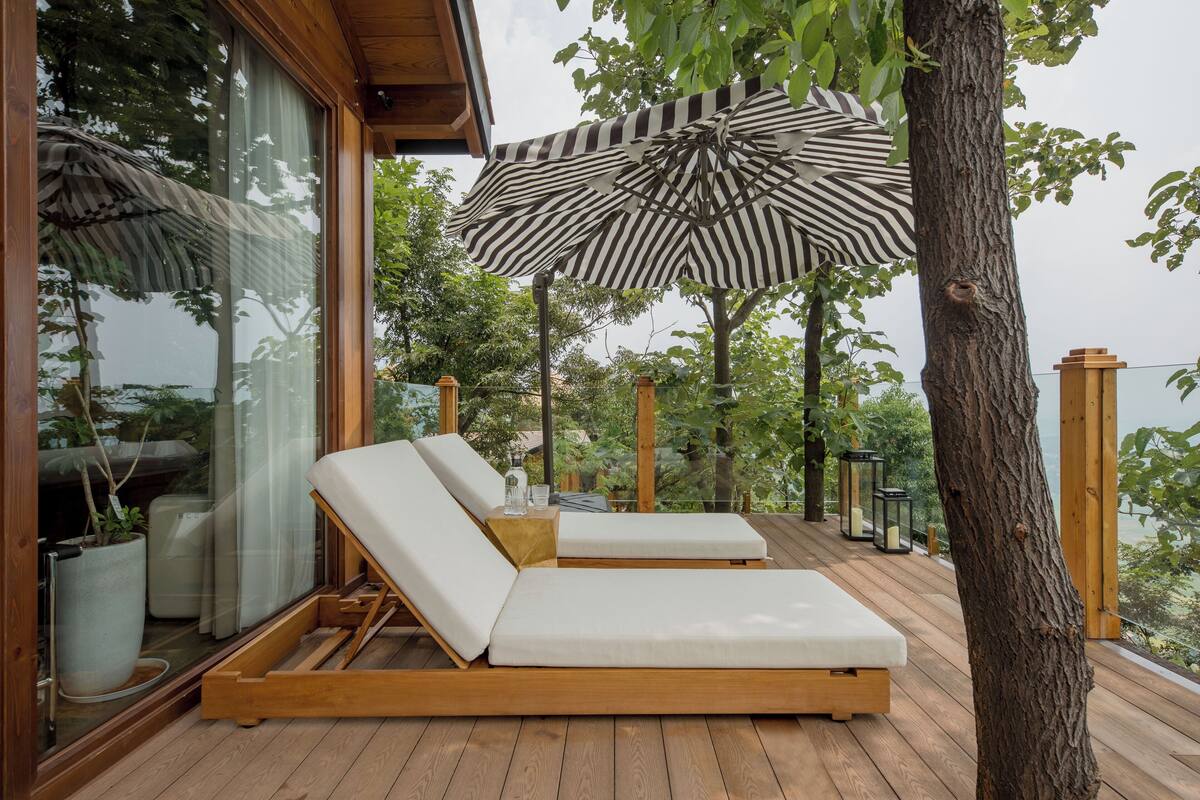 Una terraza de madera con dos sillas reclinables y un paraguas a rayas.