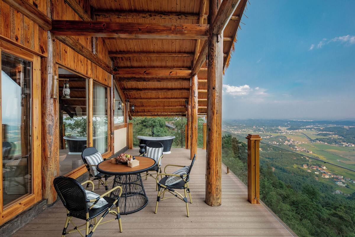Una terraza de madera con mesa y sillas, con vistas a un paisaje pintoresco.