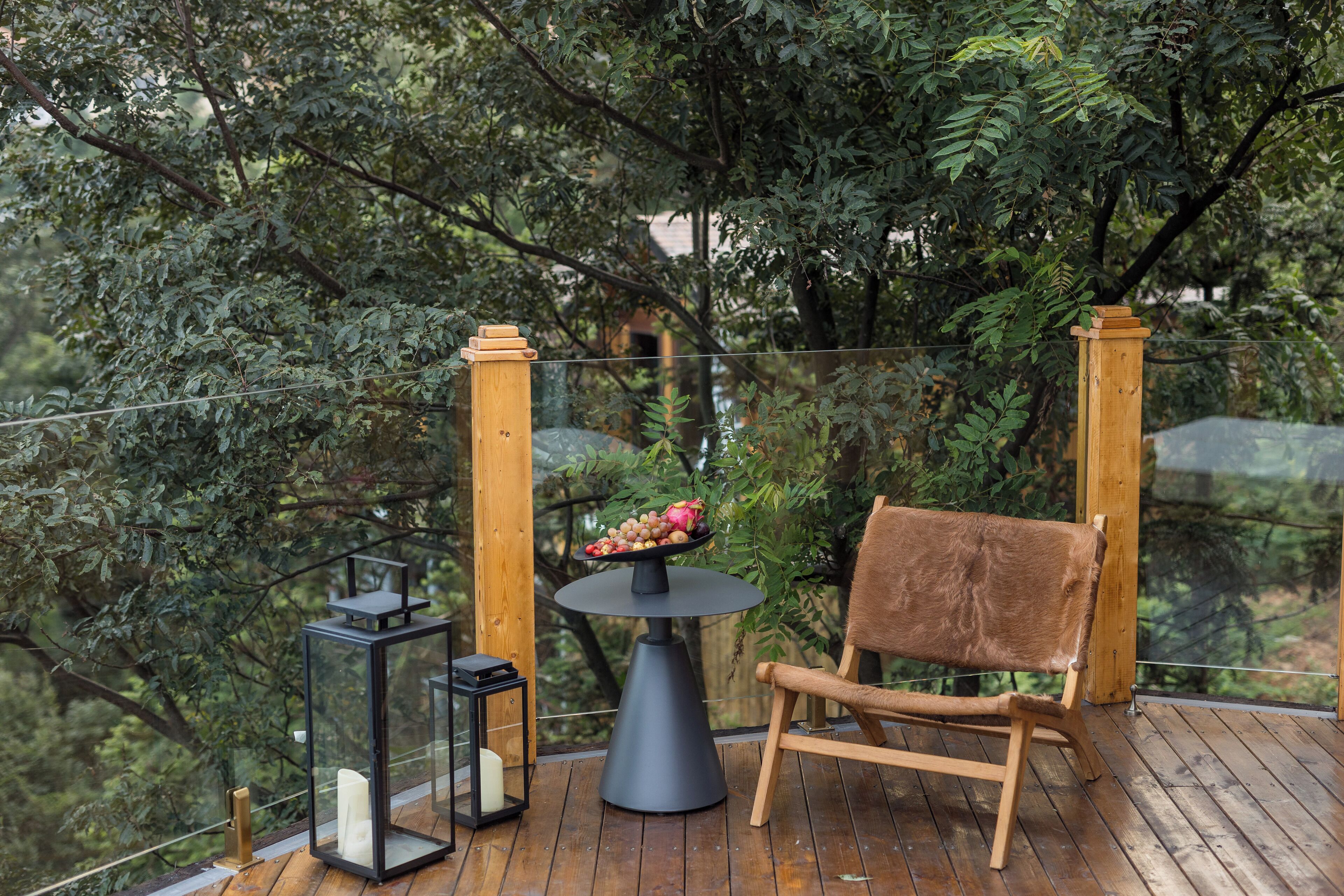 A wooden deck with a round table, a chair, and two lanterns.
