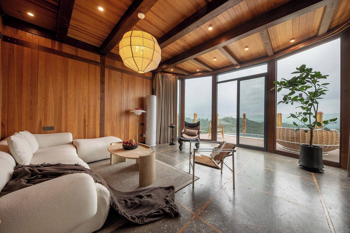 Un salón amplio con un gran ventanal, techo de madera y una planta en maceta.