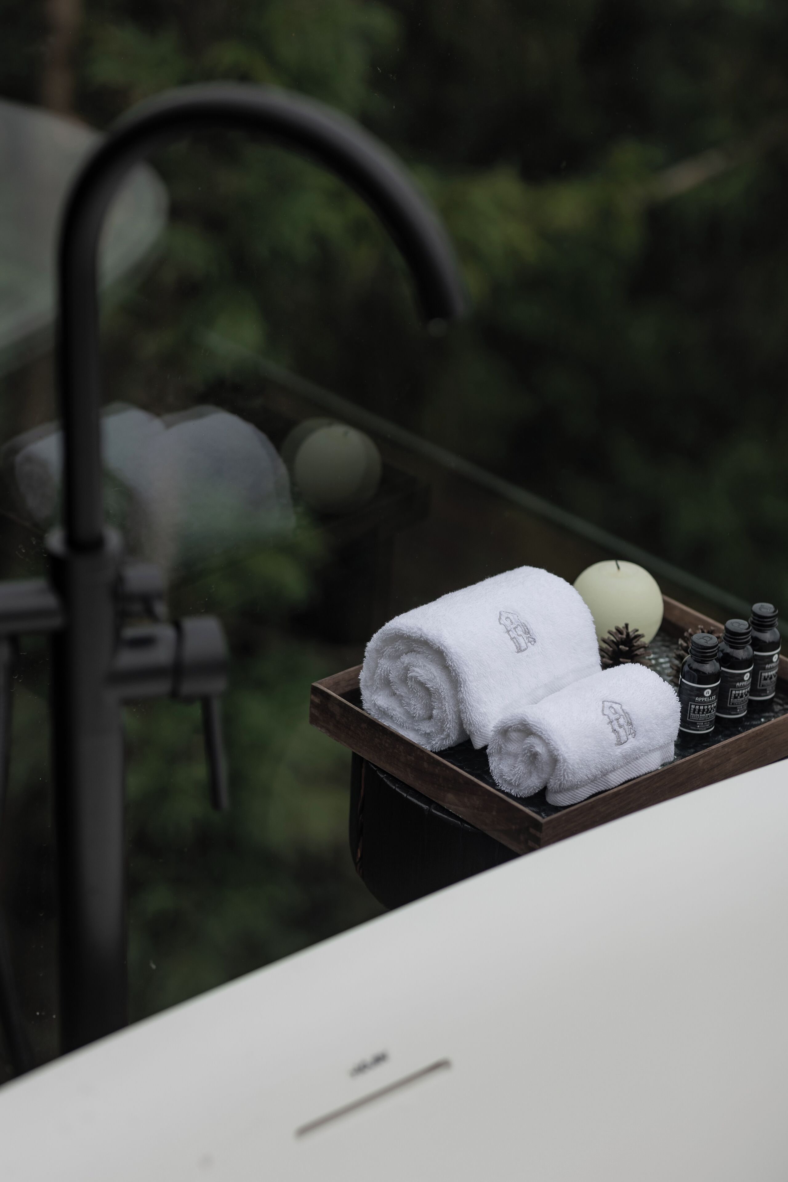 A tray with rolled towels, a candle, and essential oils on a table.