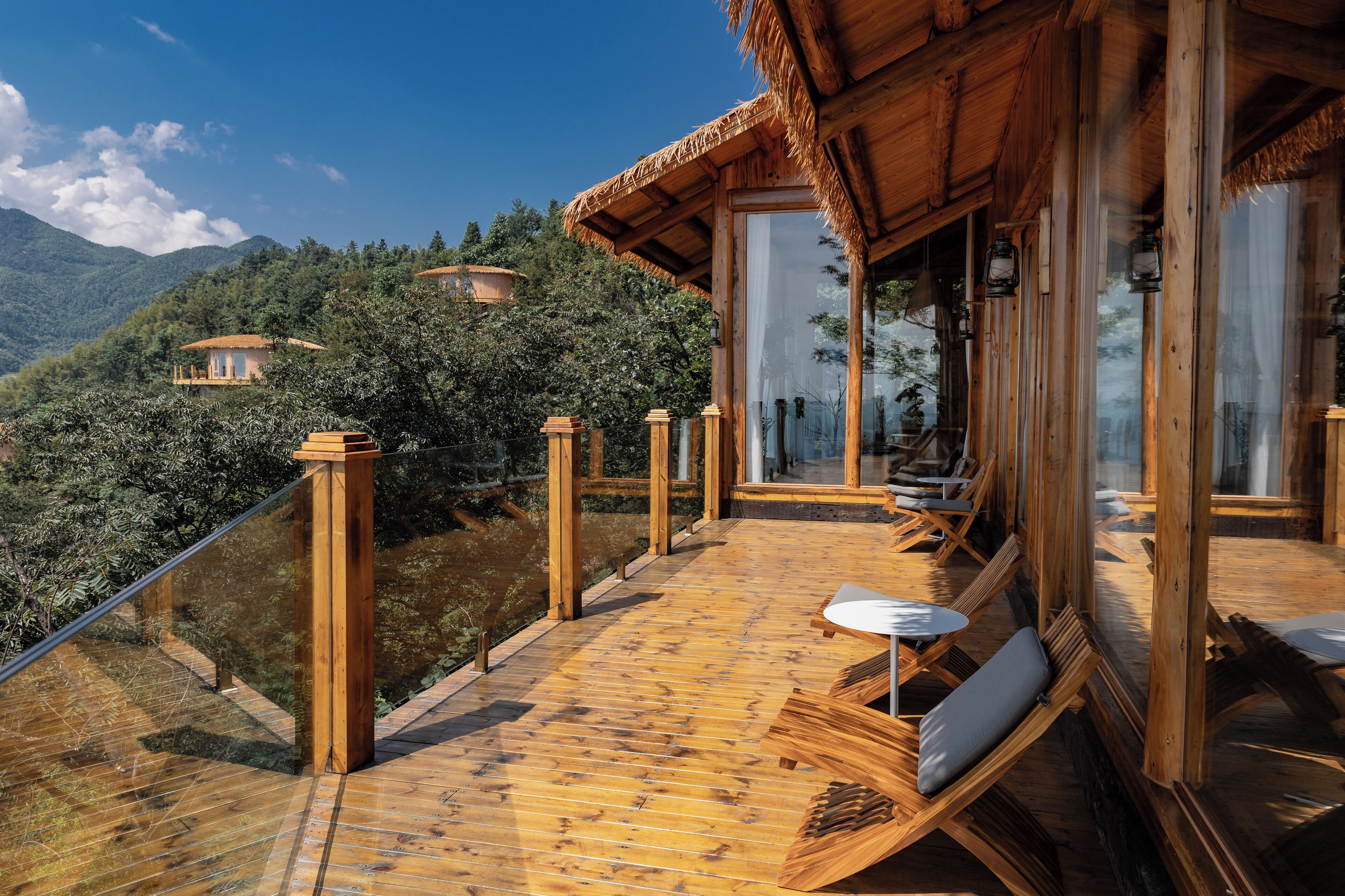 Una terraza de madera con mobiliario exterior, con vistas a un paisaje montañoso.