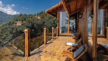 Una terraza de madera con mobiliario exterior, con vistas a un paisaje montañoso.
