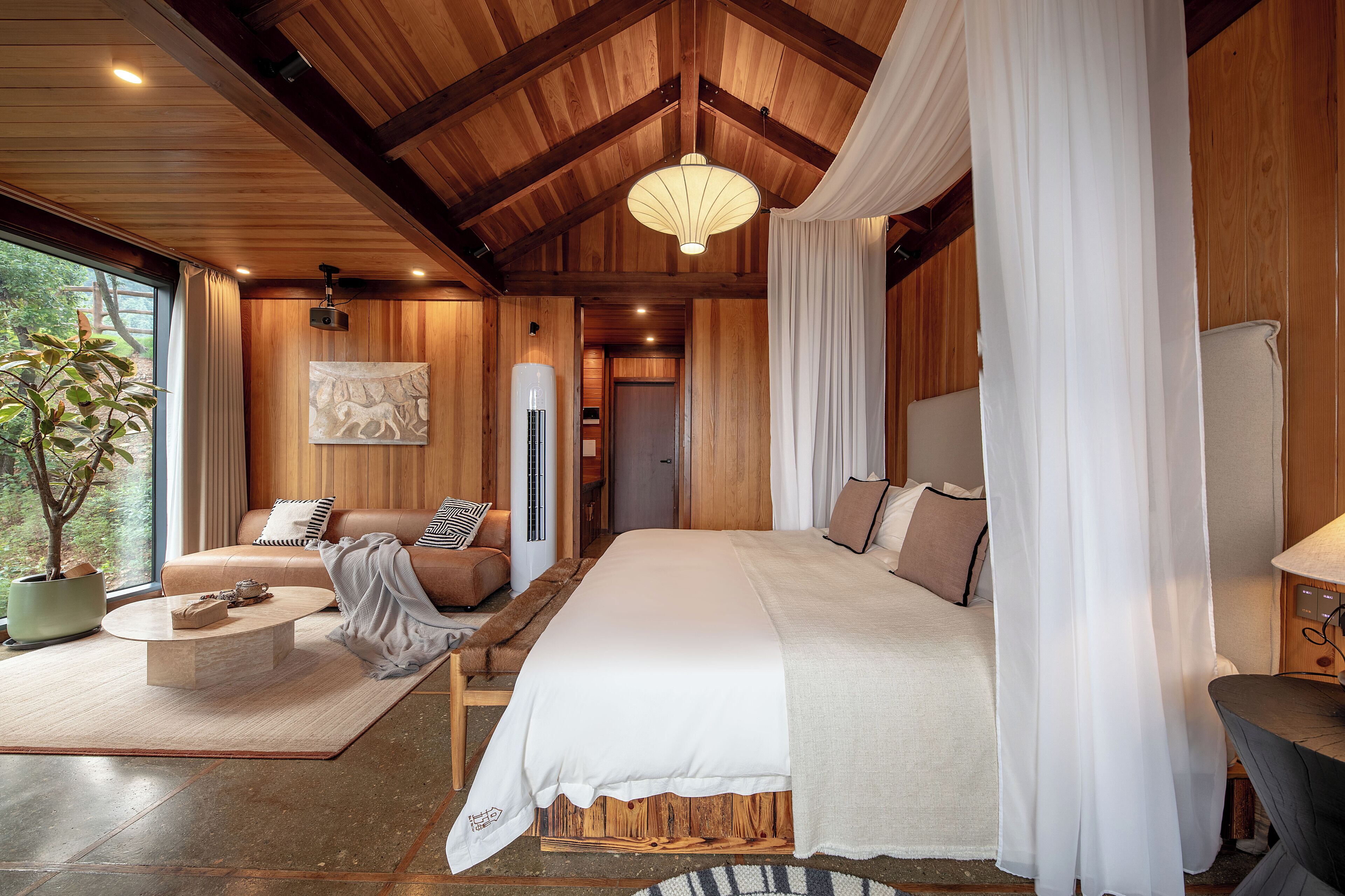 Ein geräumiges Schlafzimmer mit einem großen Bett, einer Sitzecke inklusive Sofa und Couchtisch sowie Blick auf Grünfläche.