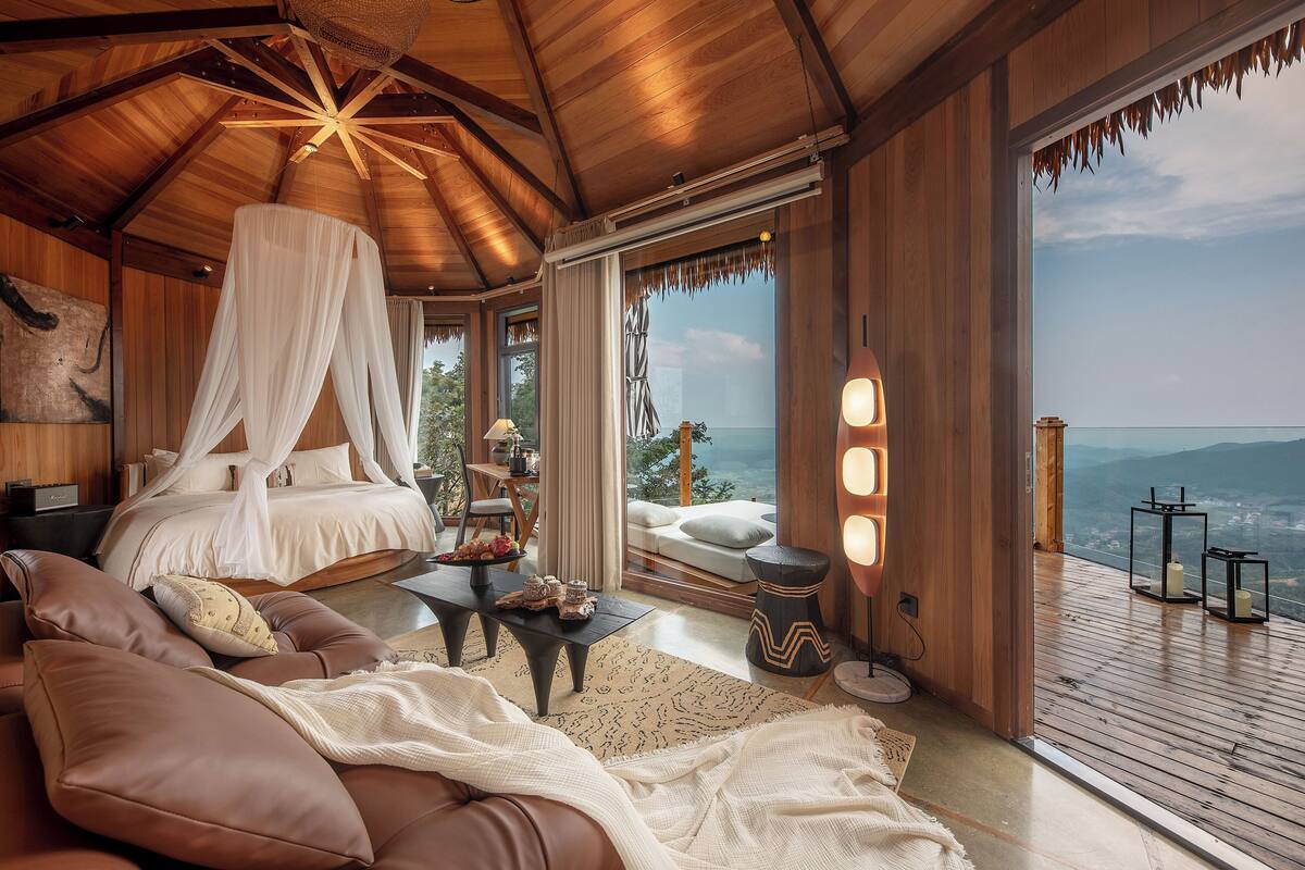 Un dormitorio con cama a dosel, un sofá, una mesita de noche y vistas al paisaje.