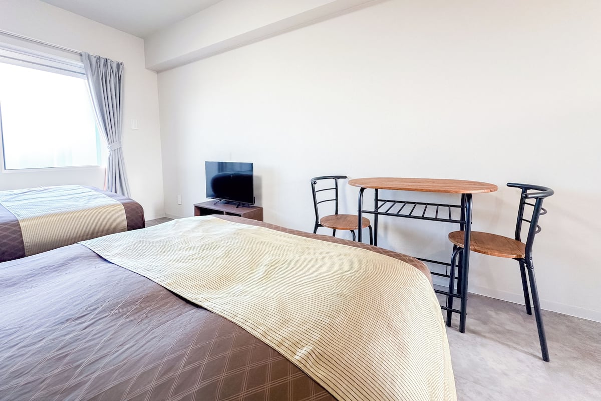 Una habitación de hotel con una cama, un televisor, una mesita pequeña y dos sillas.