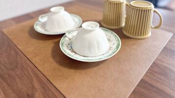 A table with two white teapots on matching saucers and two beige coffee mugs.