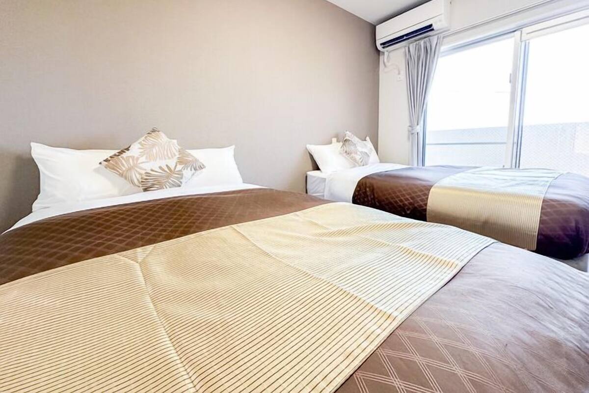 Una habitación de hotel con dos camas, un ventanal grande y un equipo de aire acondicionado.