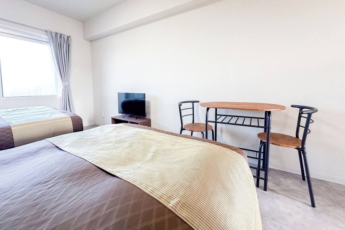 Una habitación de hotel con una cama, un televisor, una mesita pequeña y dos sillas.