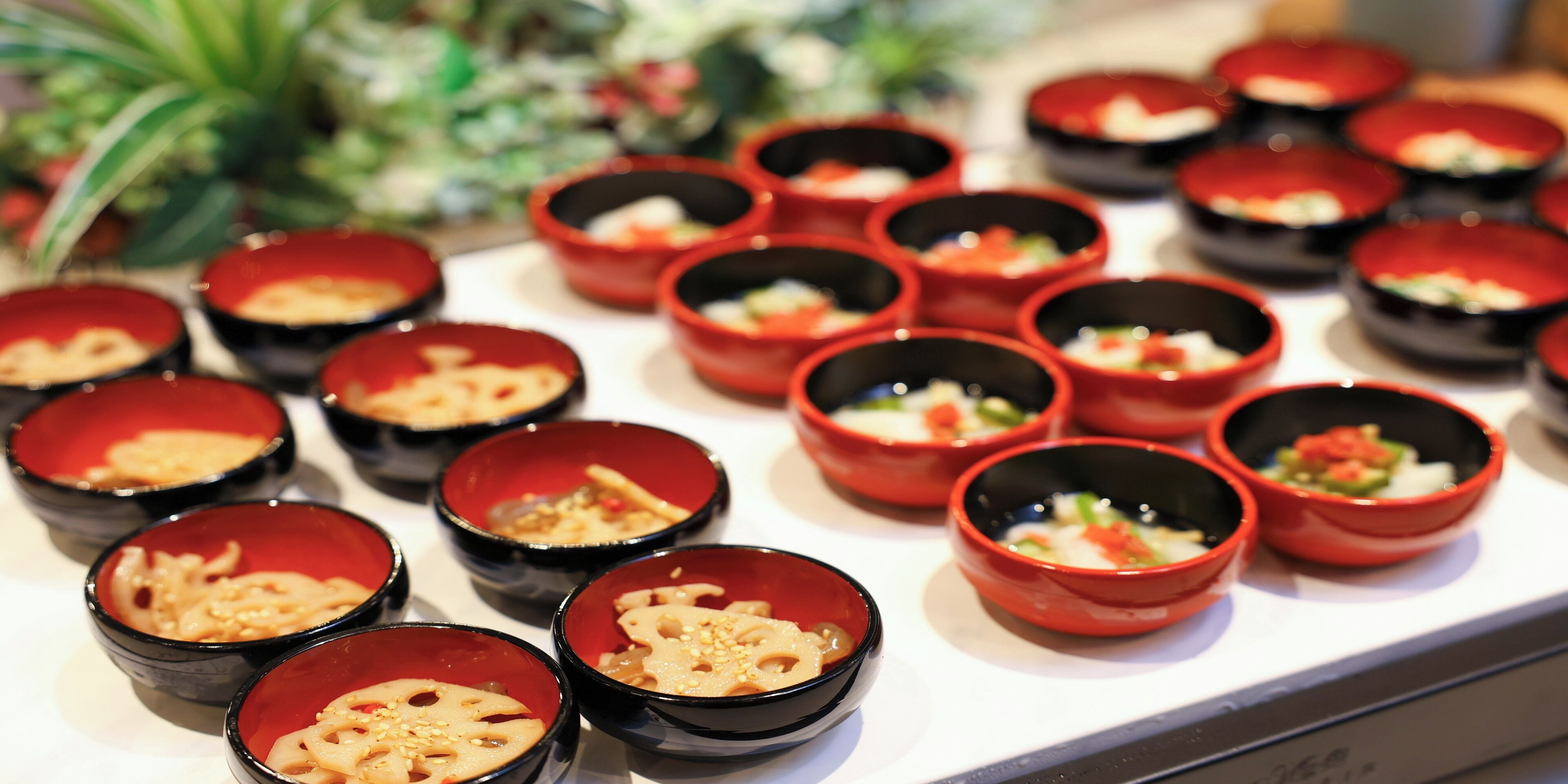 A variety of small red and black bowls containing different dishes, arranged on a table.