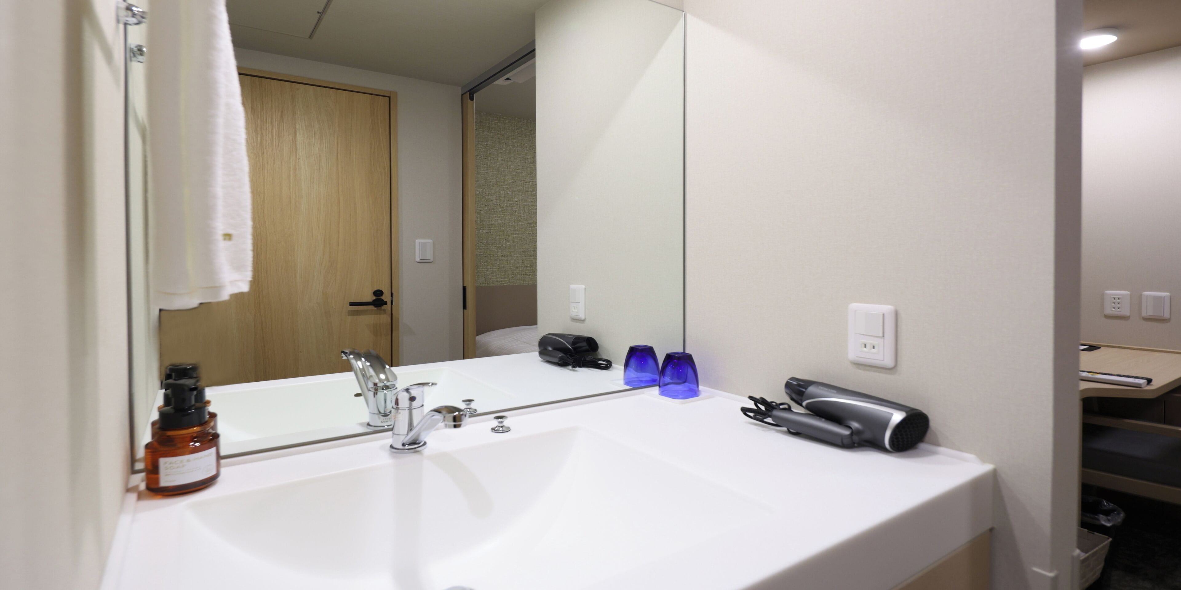 Een badkamer met een grote spiegel, een wit wastafelmeubel, een haardroger en een fles shampoo.