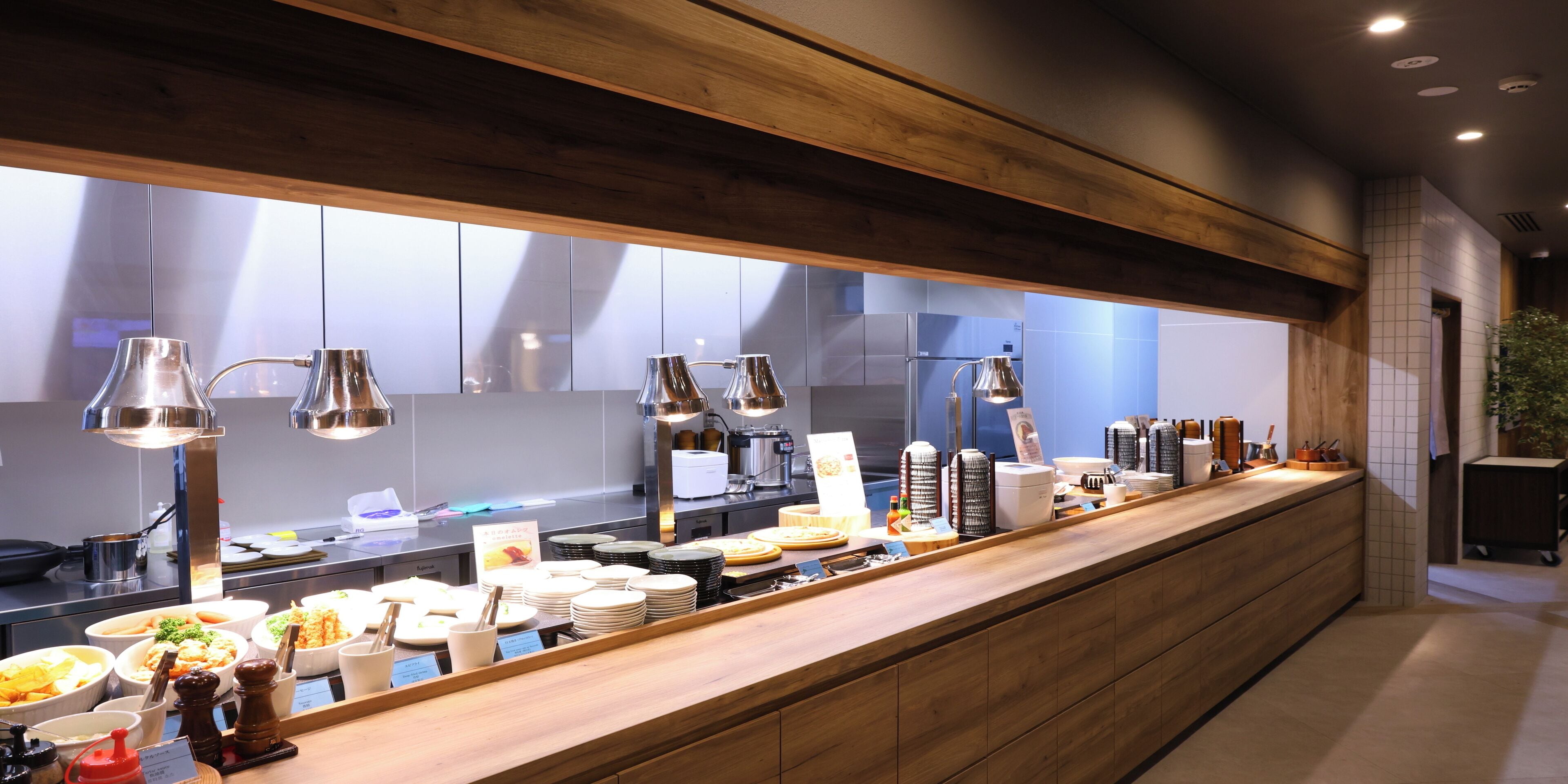 A buffet setup with various food items and utensils, a wooden counter, and overhead lighting.
