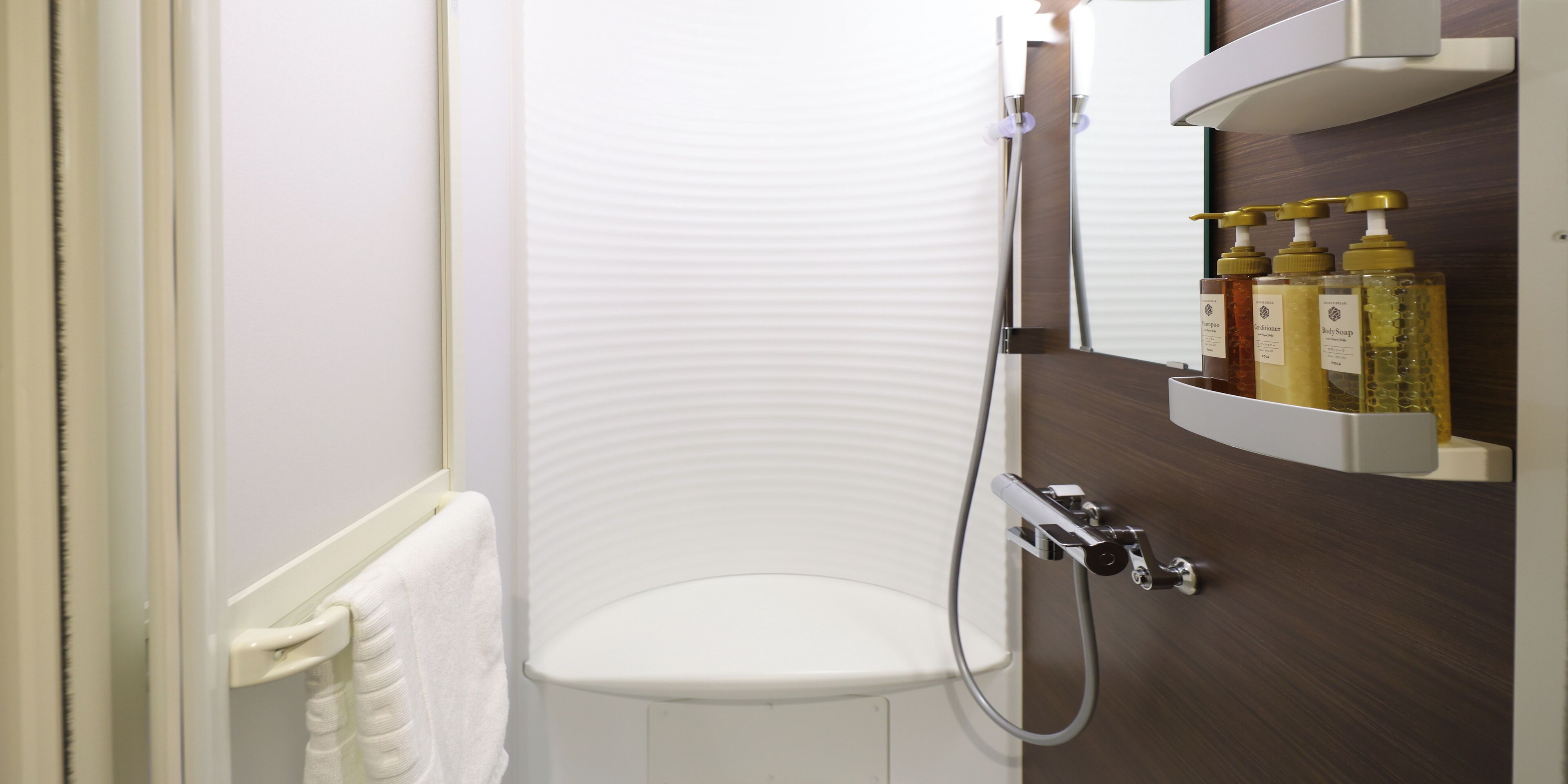 A modern bathroom with a shower enclosure, a white toilet, and a shelf with toiletries.