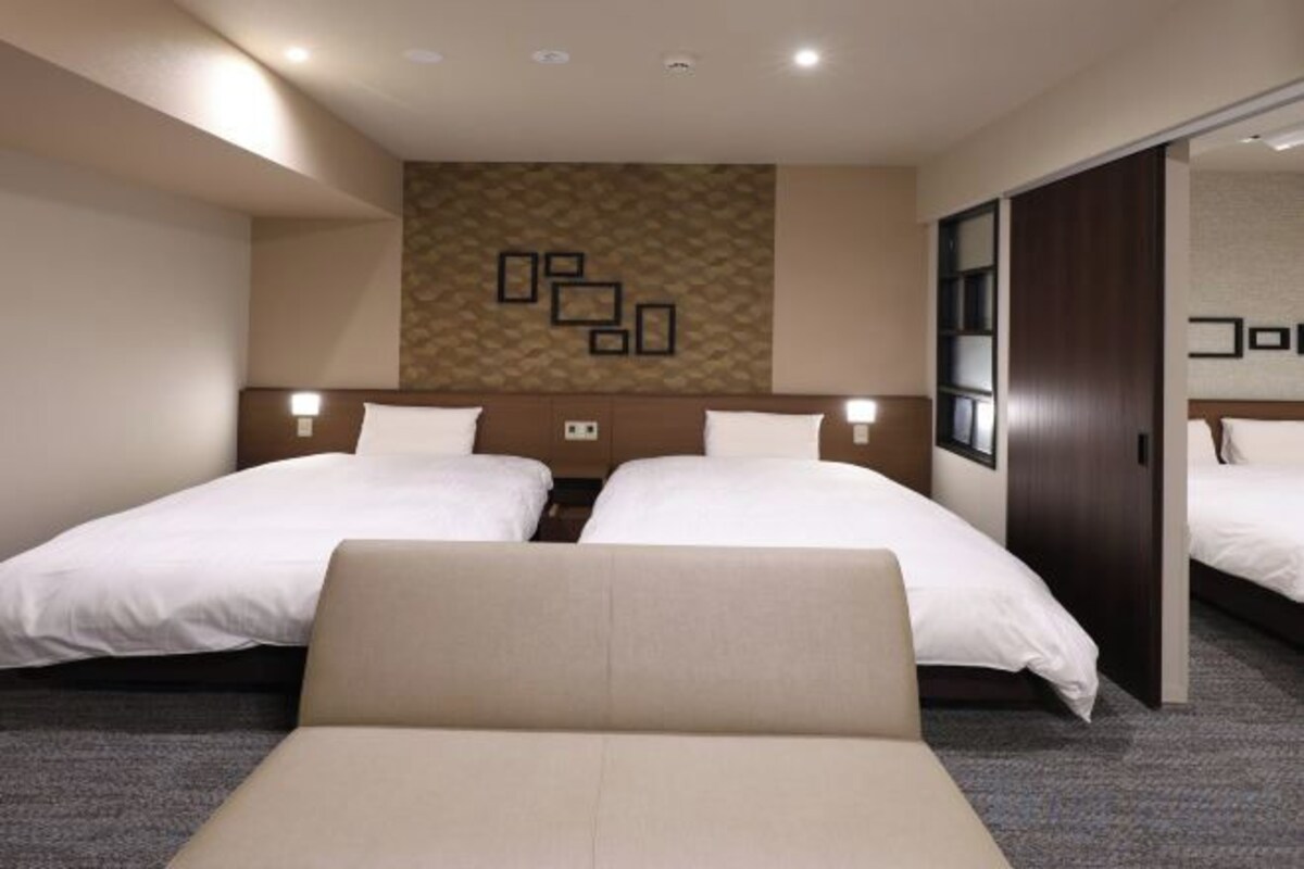 A hotel room with two beds, a sofa, a patterned wall, and a mirror.