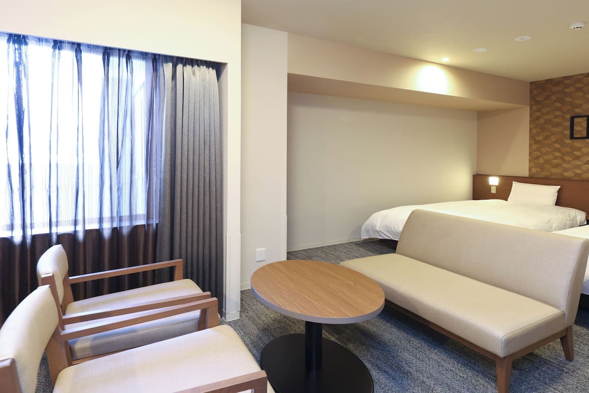 Habitación de hotel con sofá, dos camas, una mesita y una ventana con cortinas.