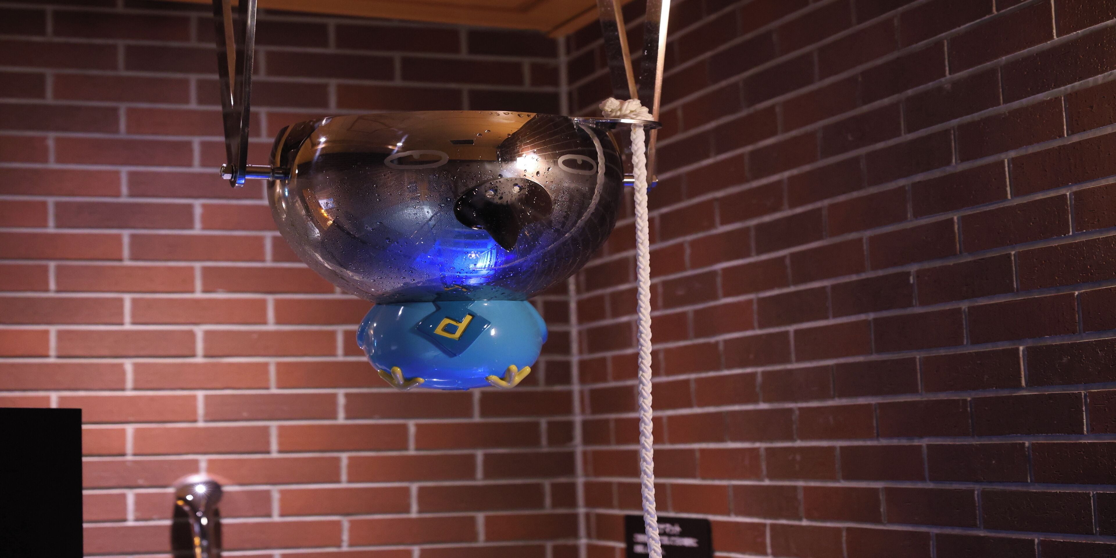 Un objet suspendu, doté d’une base bleue et d’une partie supérieure métallique, et maintenu au plafond par une corde.