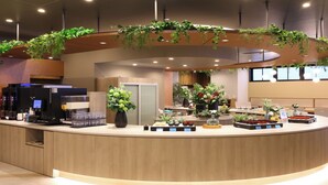A reception area with a curved counter, coffee machines, and various potted plants. - Dormy Inn Tsuruga Natural Hot Spring (Tsuruga)