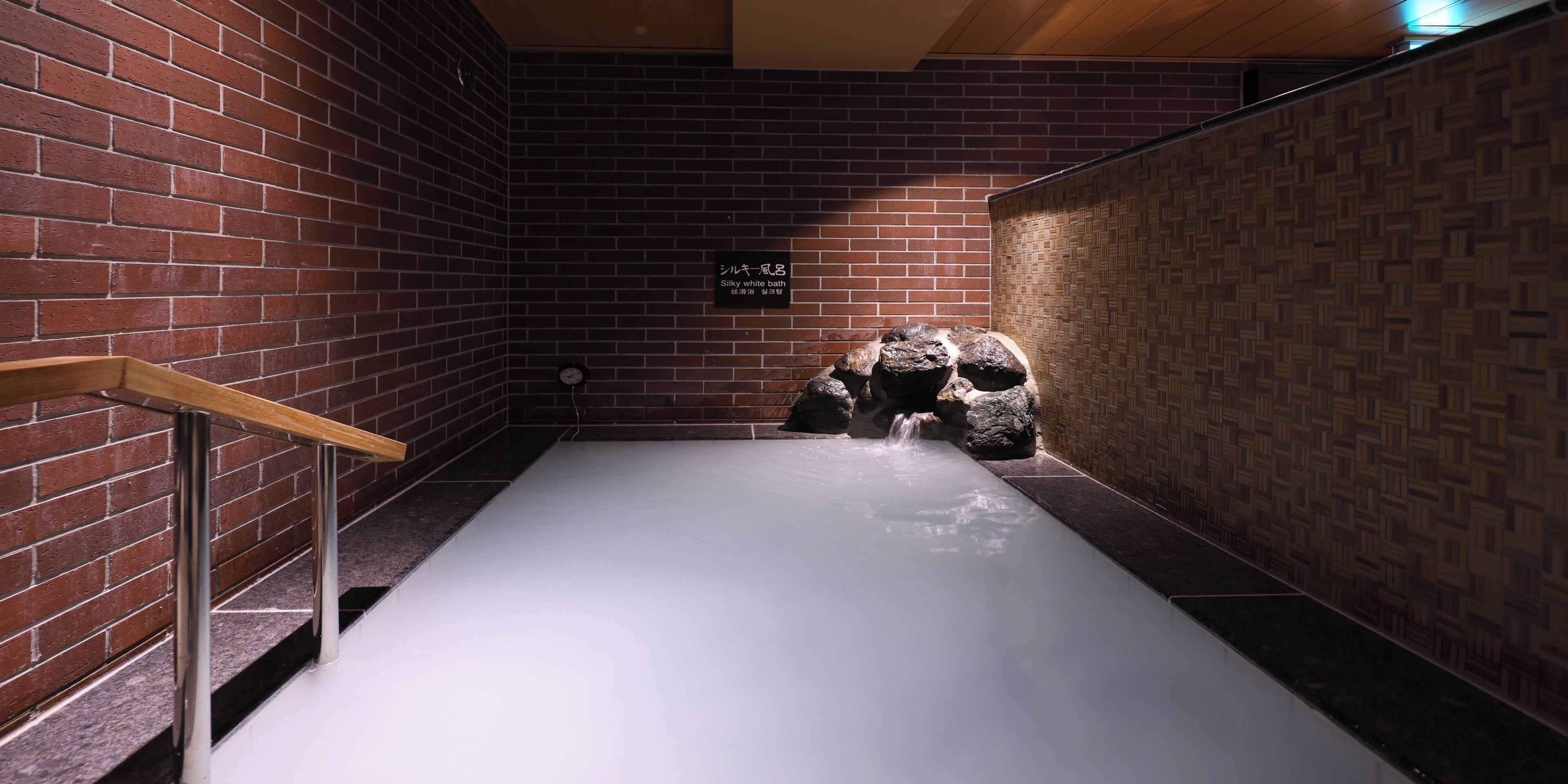 Un área de spa con una bañera de hidromasaje blanca, barandales de madera y una pared de ladrillo.