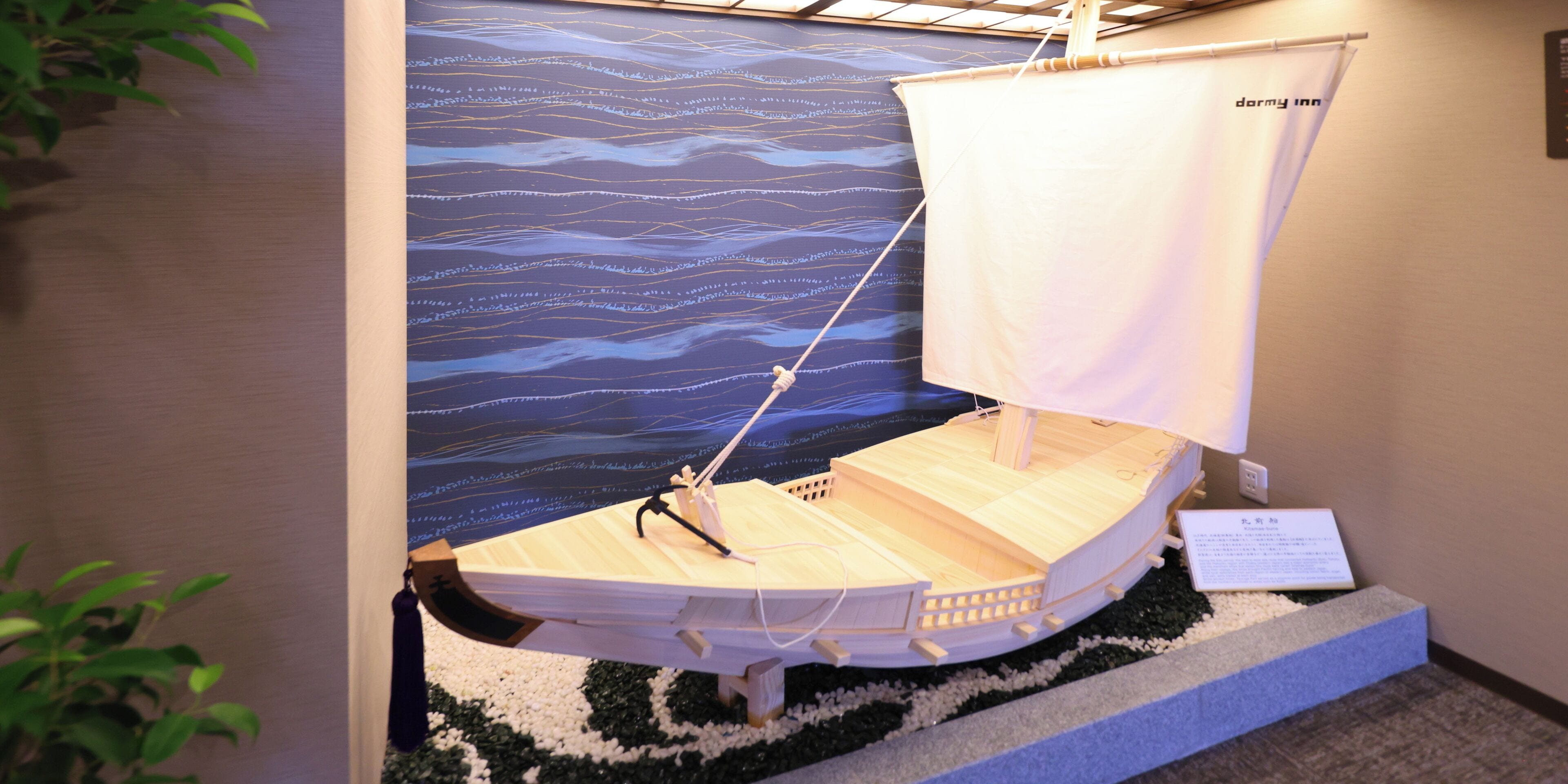 A model sailboat on display with a backdrop of ocean waves.