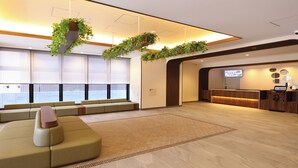 A spacious lobby with a large seating area, a reception desk, and a television screen. - Dormy Inn Tsuruga Natural Hot Spring (Tsuruga)