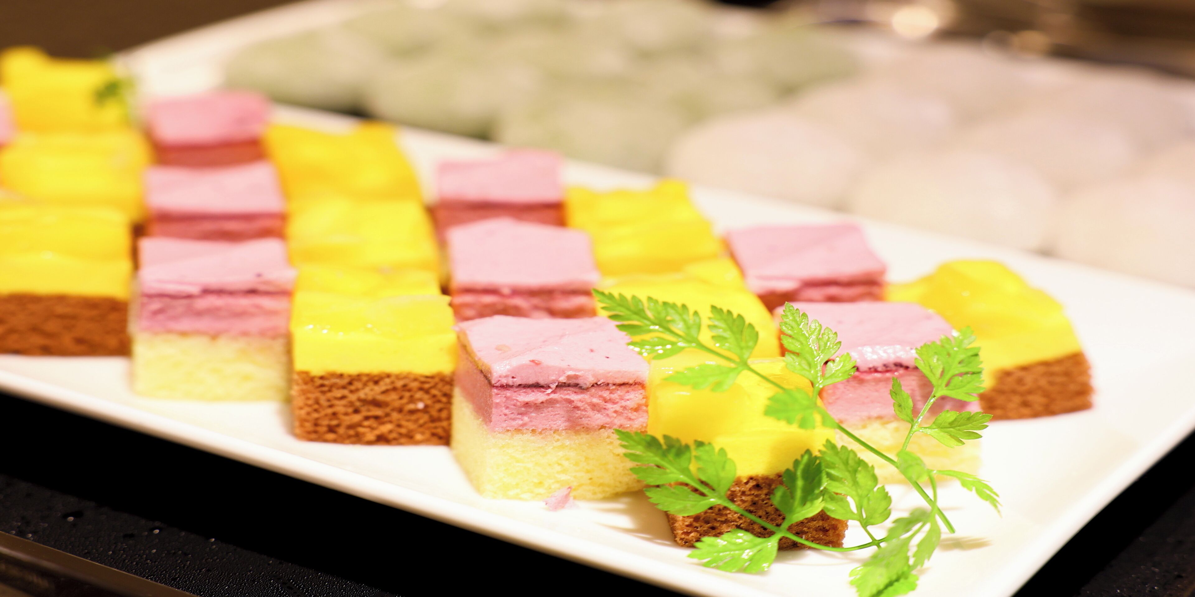 Un plato blanco rectangular con trozos cuadrados de pastel en capas, adornado con una ramita de perejil.