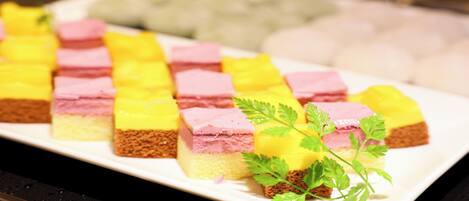 A white rectangular plate with neatly arranged square pieces of layered cake, garnished with a sprig of parsley.