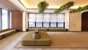 A spacious lobby with a large seating area, a reception desk, and large windows with blinds. - Dormy Inn Tsuruga Natural Hot Spring (Tsuruga)