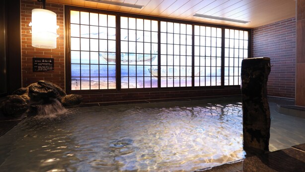 A hot spring area with a view of boats through a large window, a wooden structure, and a stone fountain. - Dormy Inn Tsuruga Natural Hot Spring (Tsuruga)