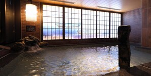 A hot spring area with a view of boats through a large window, a wooden structure, and a stone fountain. - Dormy Inn Tsuruga Natural Hot Spring (Tsuruga)