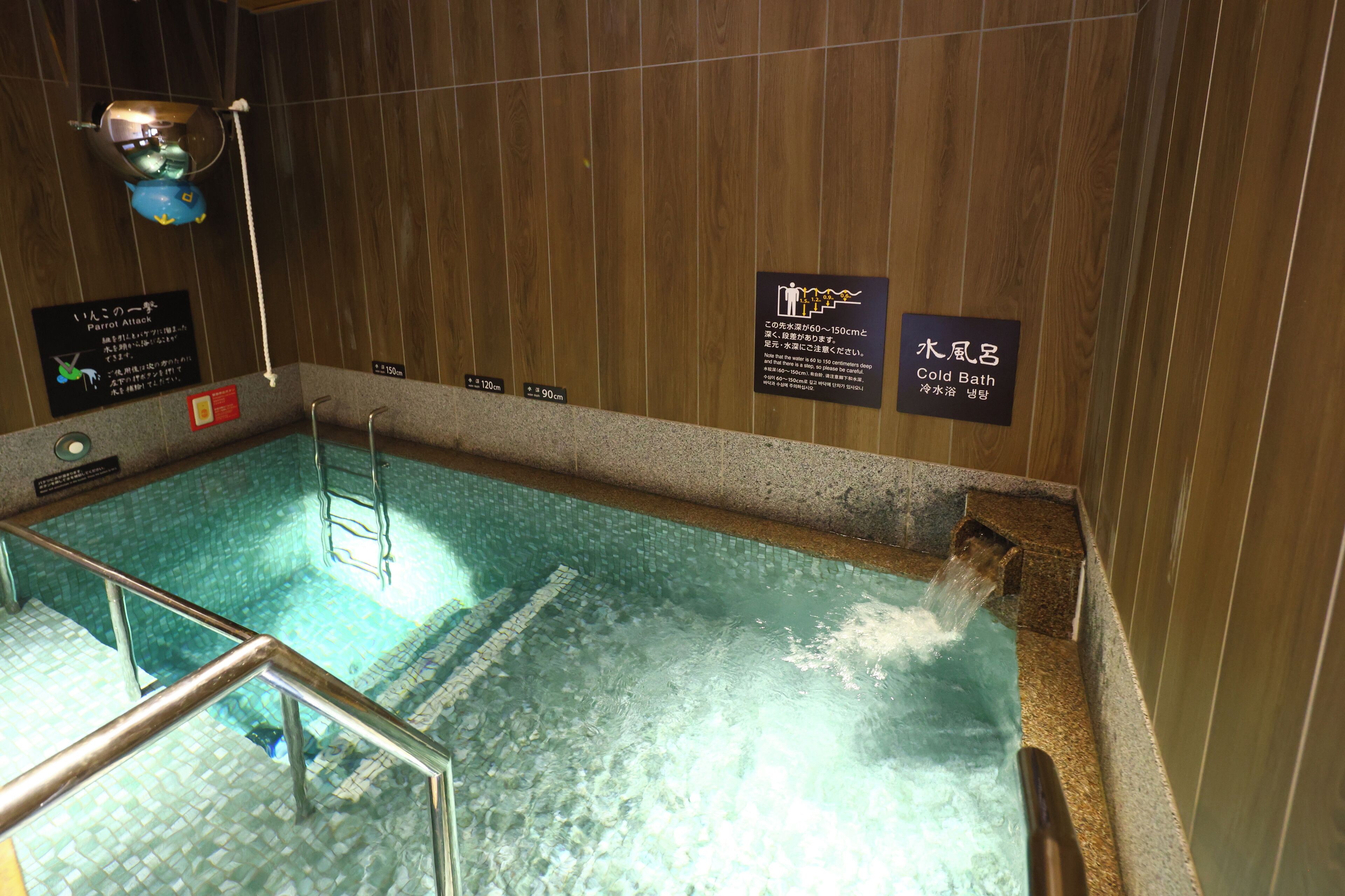 A hot tub with wooden walls and a tiled floor. There are signs indicating the depth of the water and a warning about the water temperature.
