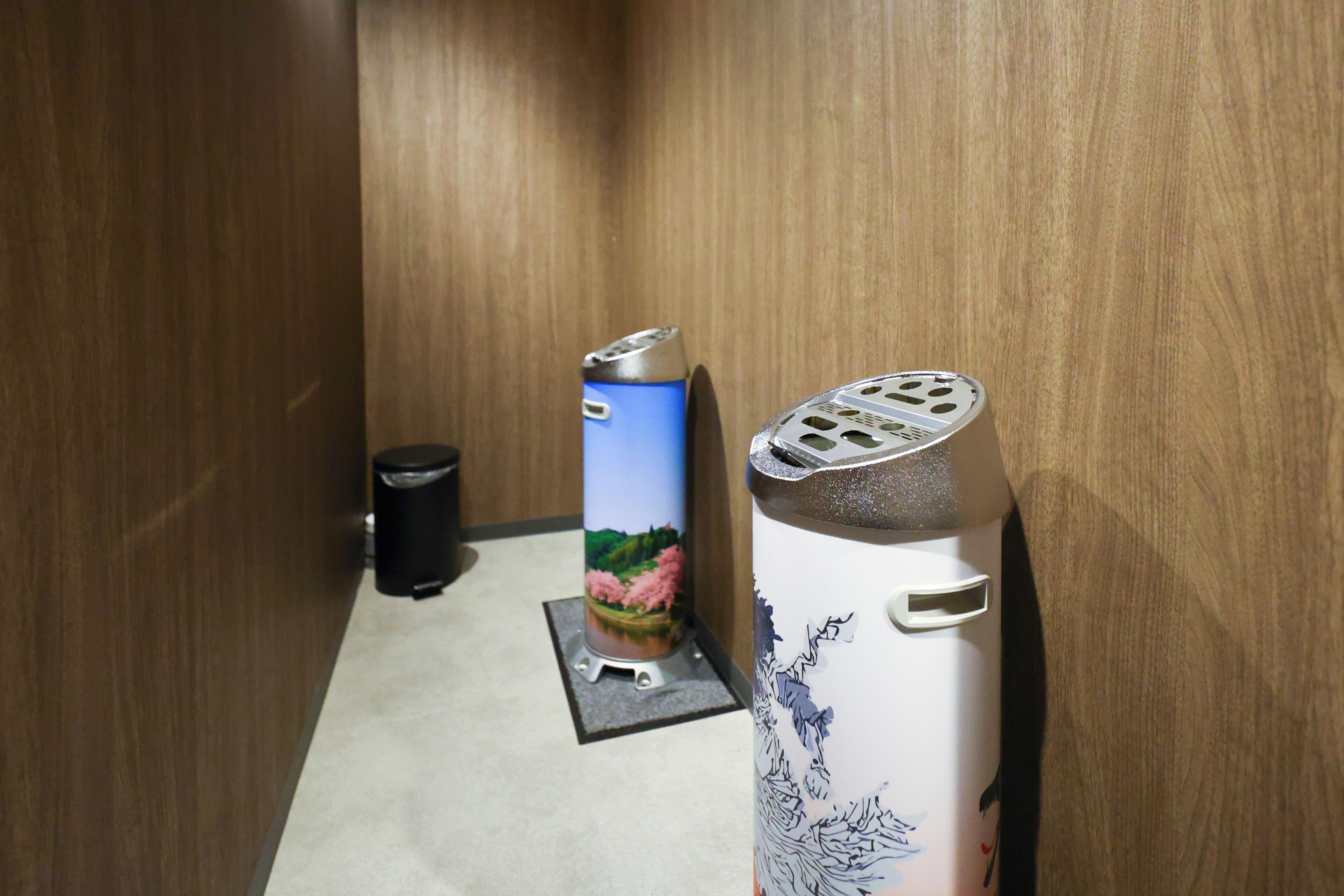 A narrow hallway with a trash bin, a blue can with a landscape design, and a white can with a tree design.