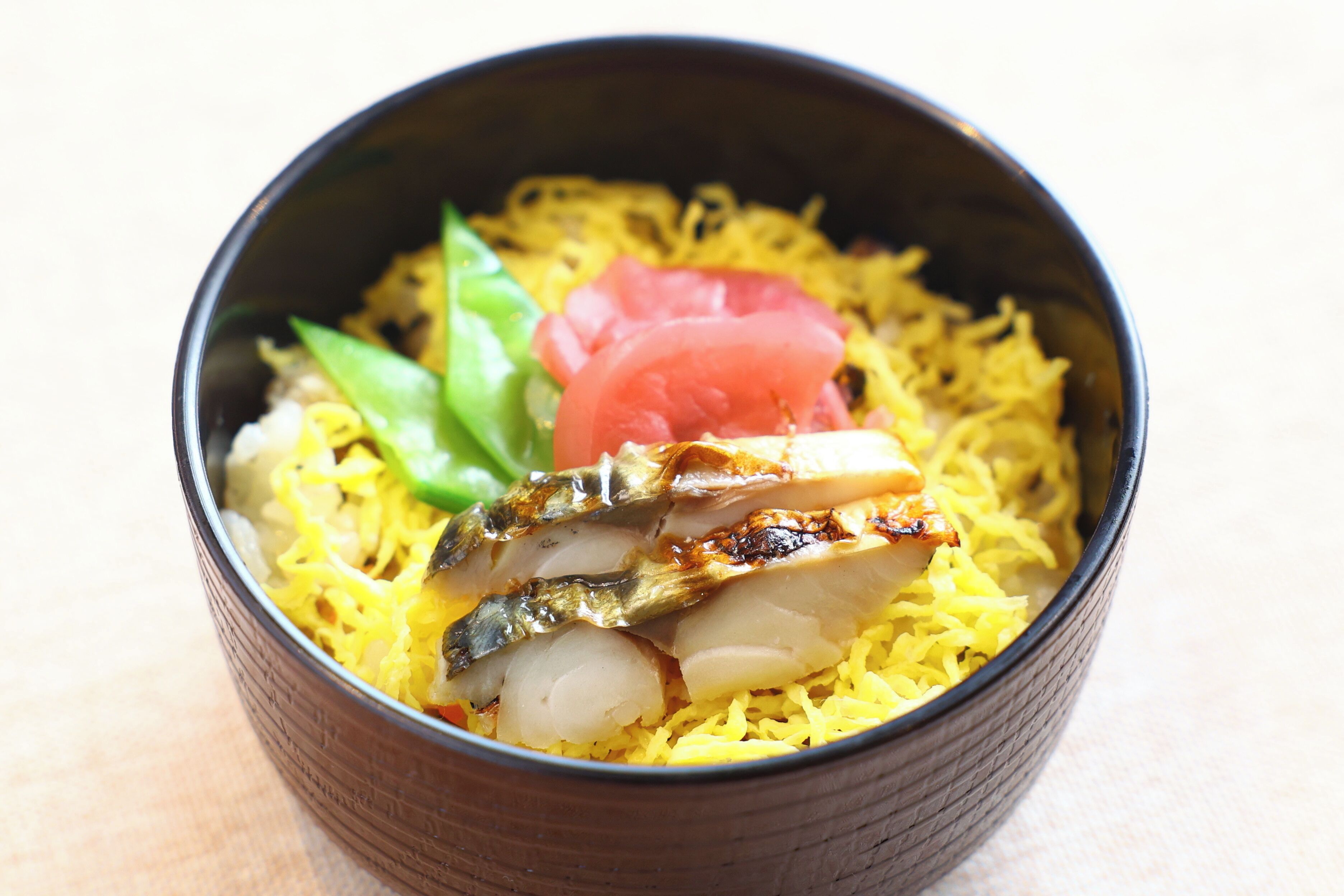 A bowl of food with rice, fish, and vegetables.