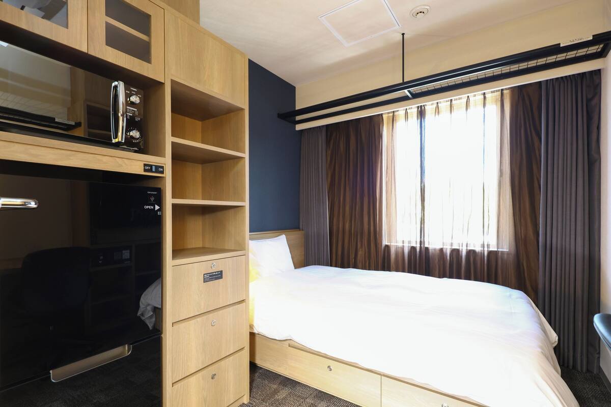 A hotel room with a bed, a wardrobe, a microwave, and a window with curtains.