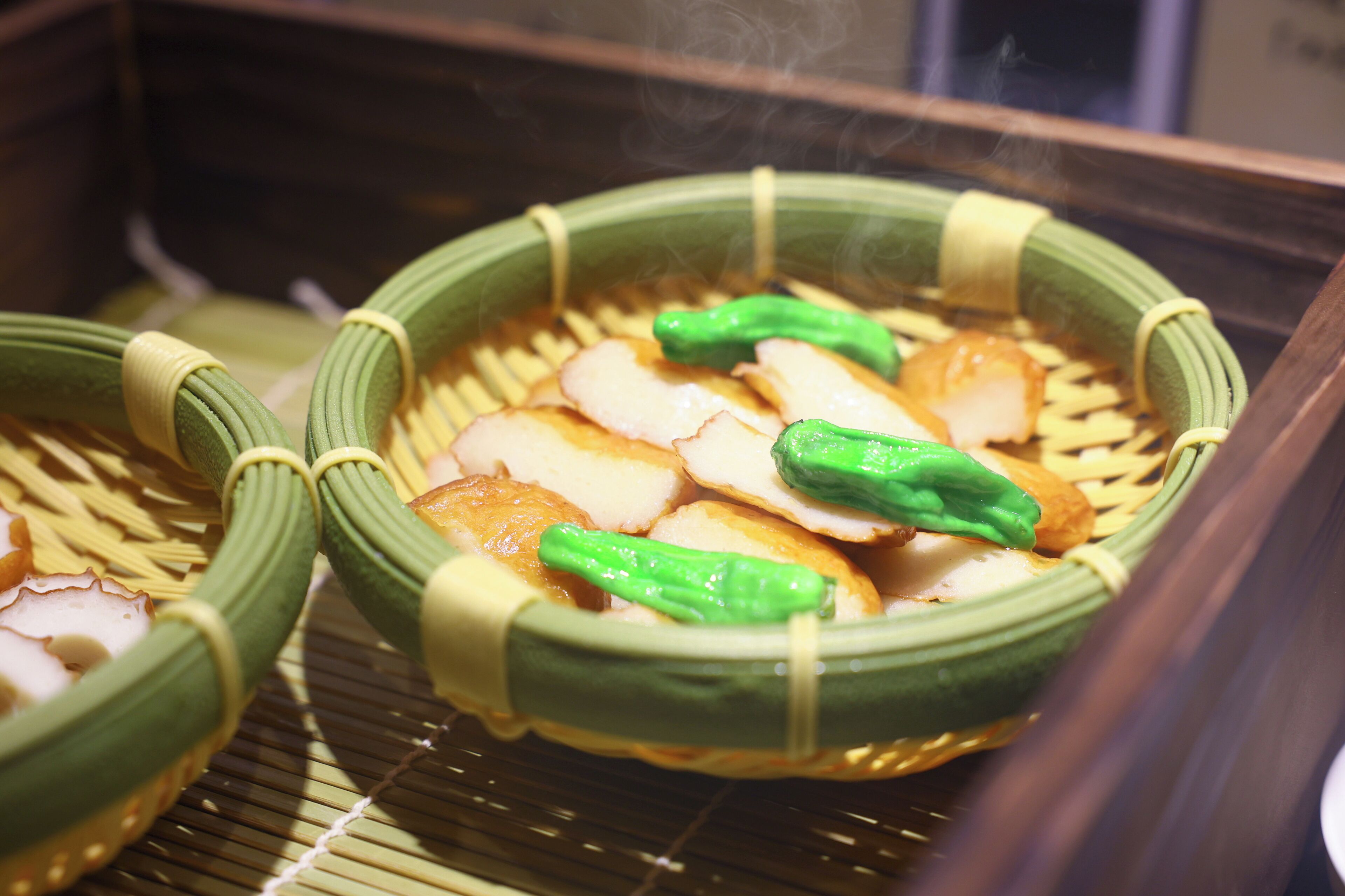 A traditional Japanese dish with bamboo baskets, green vegetables, and slices of fish.