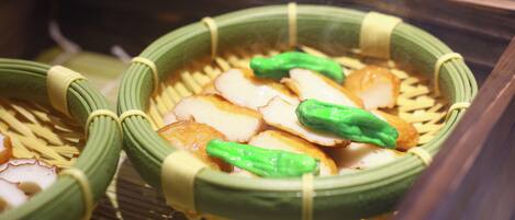 A traditional Japanese dish with bamboo baskets, green vegetables, and slices of fish.