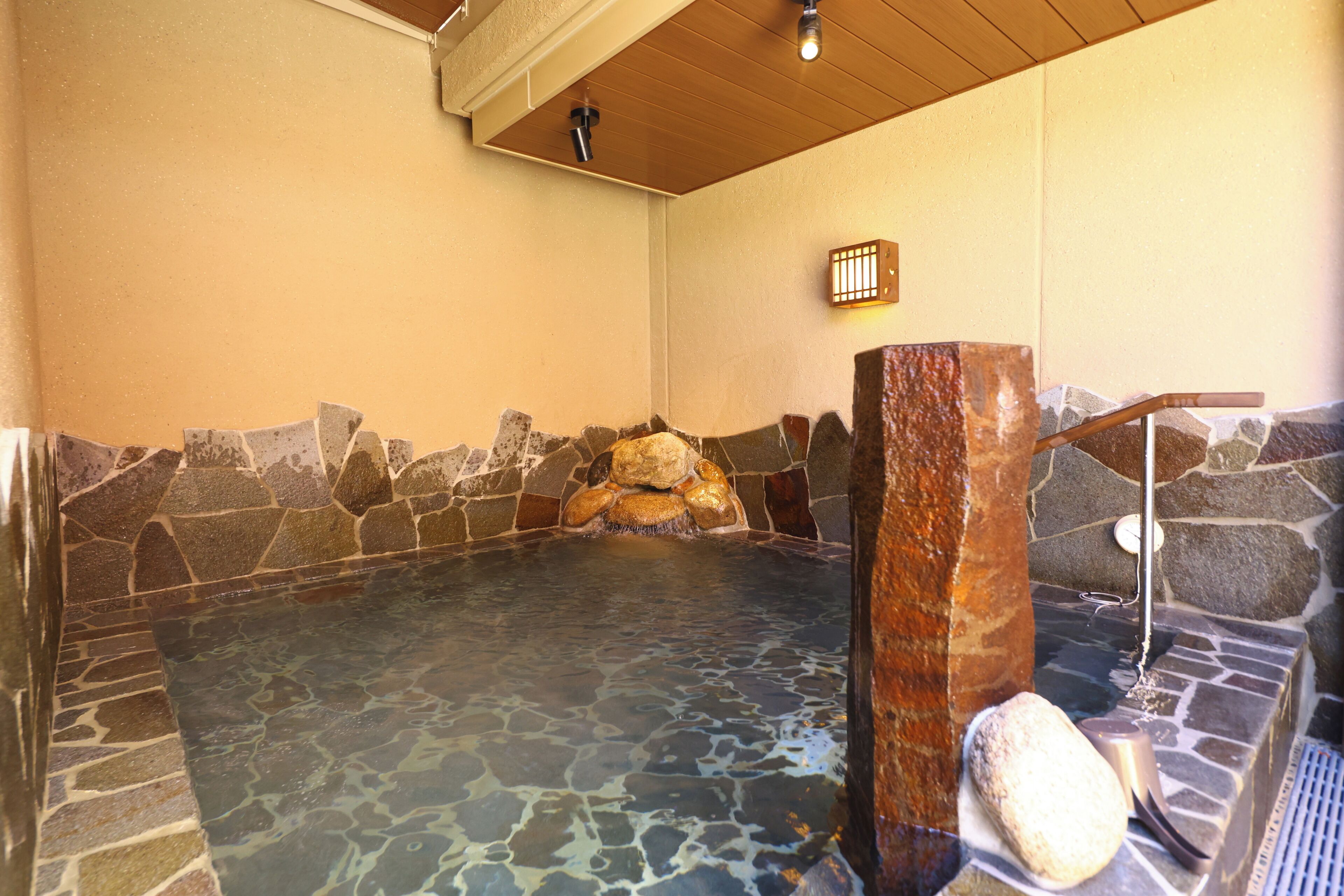 A stone-walled hot spring bath with a wooden ceiling and a stone bench.