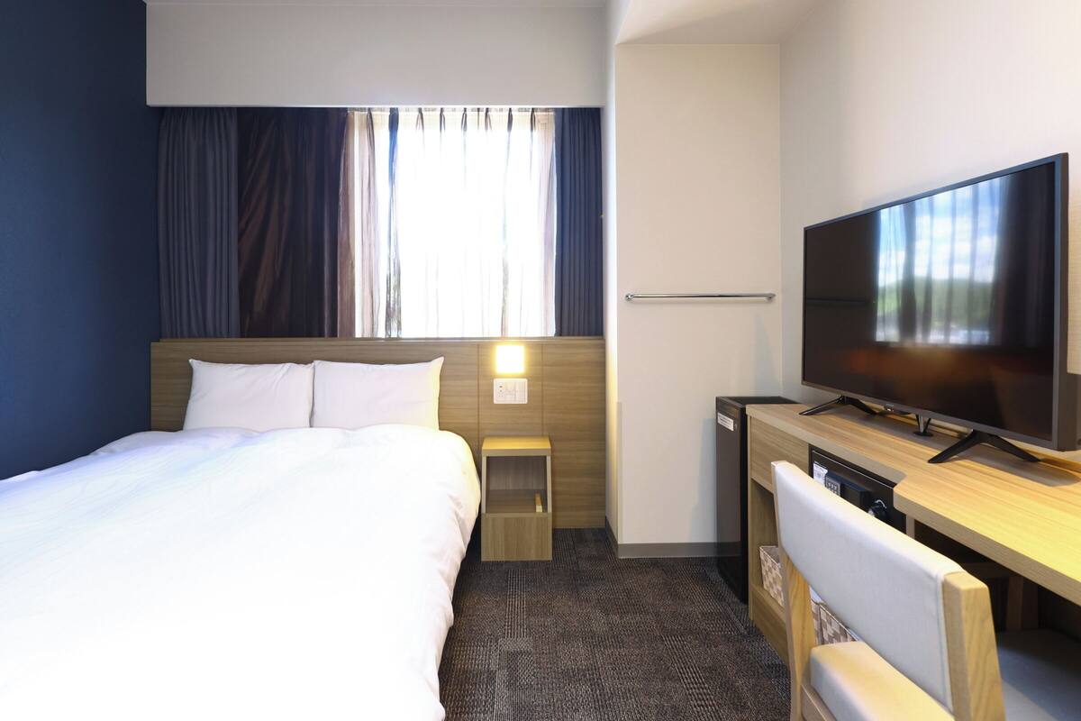A hotel room with a bed, a desk, a television, and a window with curtains.