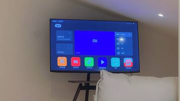 A flat-screen TV mounted on a stand against a wall, displaying a user interface with various app icons.