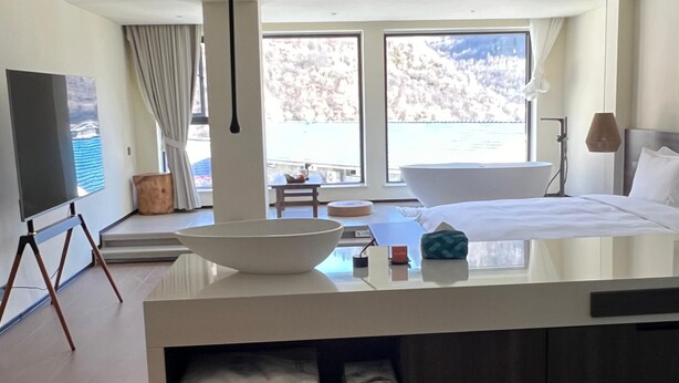 A modern hotel room with a large window, a bathtub, a flat-screen TV, and a dining area. - Harmony Zen Retreat in Jiuzhai Valley (Ngawa Autonomous Prefecture)