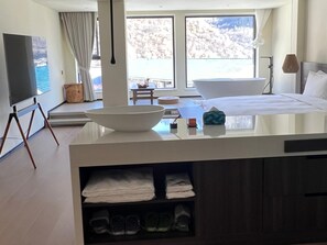 Ein modernes Hotelzimmer mit großem Fenster, einer Badewanne, einem Flachbildfernseher und einem Essbereich.