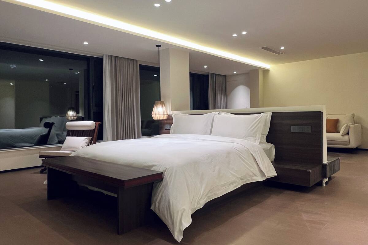 Une chambre d’hôtel moderne dotée d’un grand lit, de tables de chevet, d’un coin salon et d’une grande fenêtre donnant sur un paysage agréable.