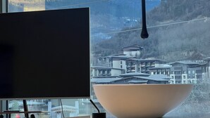 A room with a large window overlooking a mountainous landscape, a modern desk with a flat-screen TV, and a large beige bowl on the windowsill. - Harmony Zen Retreat in Jiuzhai Valley (Ngawa Autonomous Prefecture)
