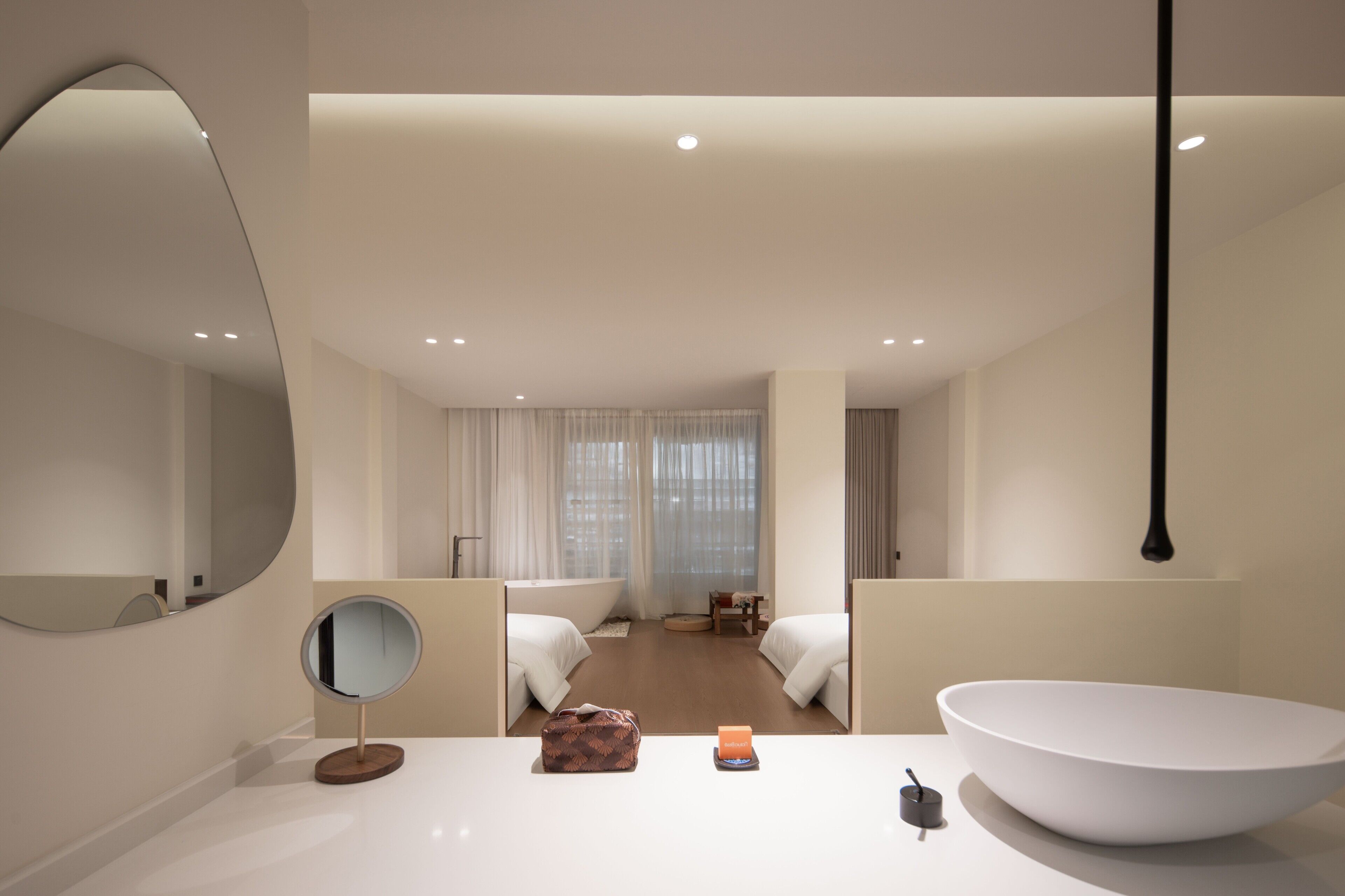 A modern hotel room with a large round mirror, a white sink, and two beds.