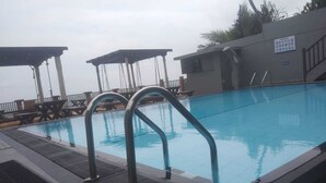 A swimming pool with metal handrails, a covered seating area, and a building with a sign in the background. - Rock Fort Beach Resort (Unawatuna)