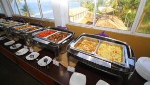 A buffet with various food options and a view of the ocean and palm trees through large windows. - Rock Fort Beach Resort (Unawatuna)