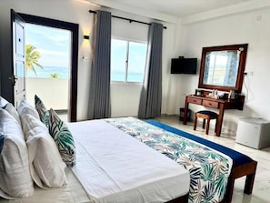 A hotel room with a bed, a desk, a chair, a television, and a view of the ocean. - Rock Fort Beach Resort (Unawatuna)