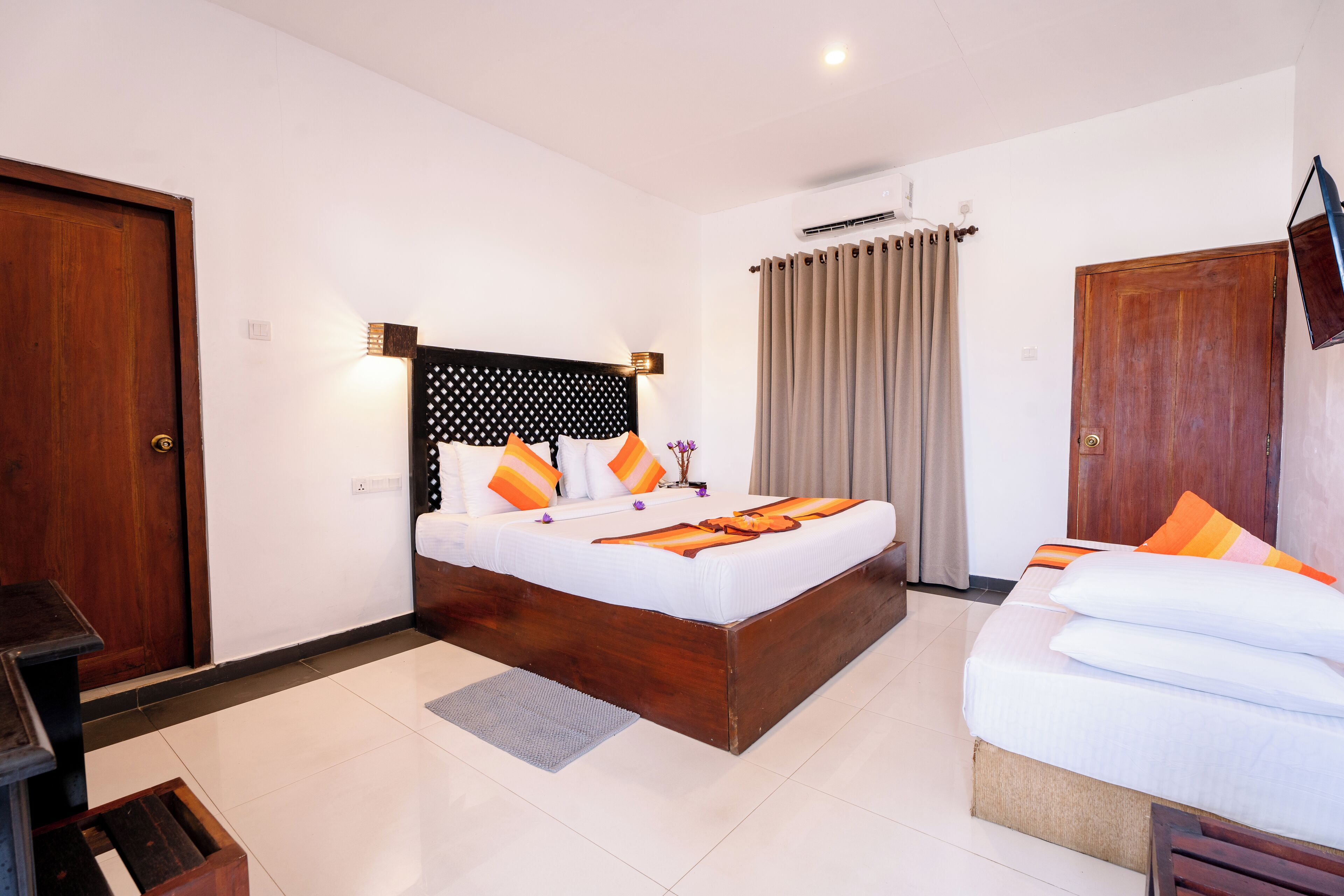 A hotel room with a large bed, a wooden headboard, a television mounted on the wall, and a window with curtains.