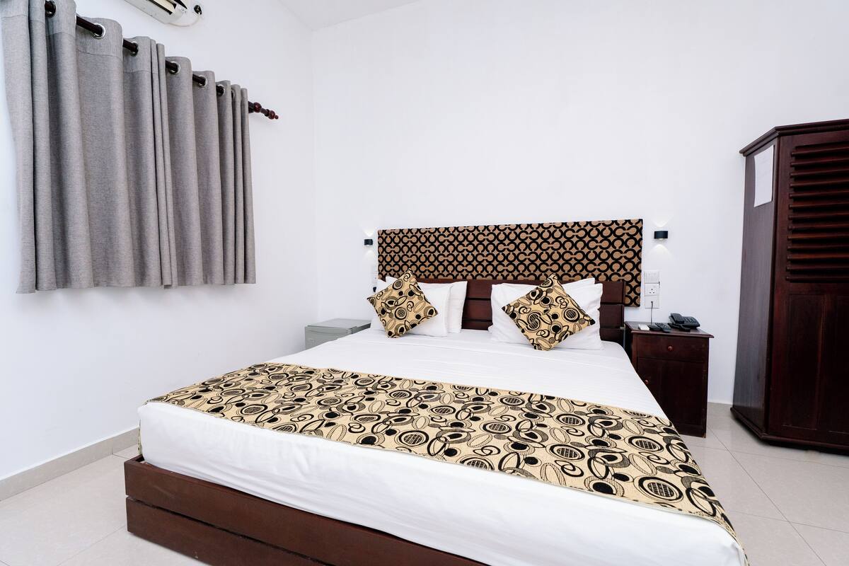 A neatly made bed with a patterned bedspread, a wooden headboard, and a bedside table with a phone.